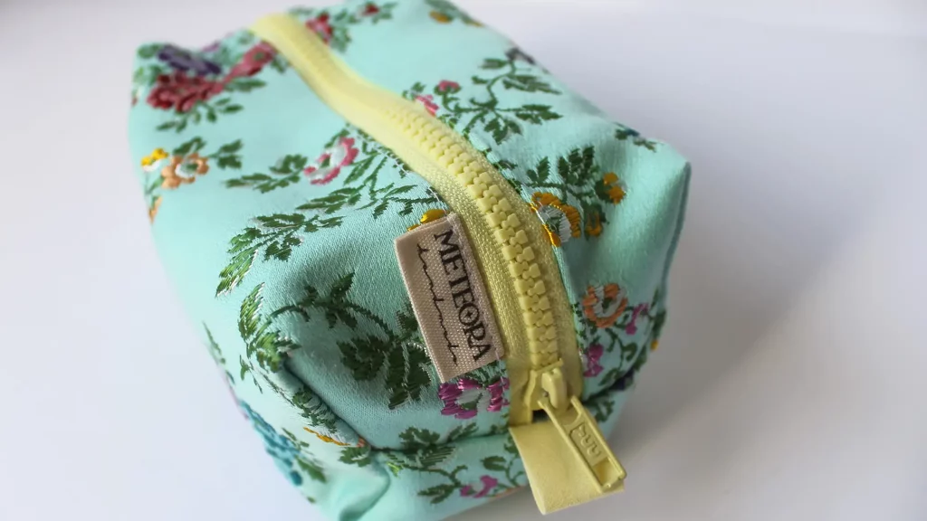 Neceser cuadrado de tela verde menta con estampado floral multicolor y cremallera amarilla de Meteora Handmade.