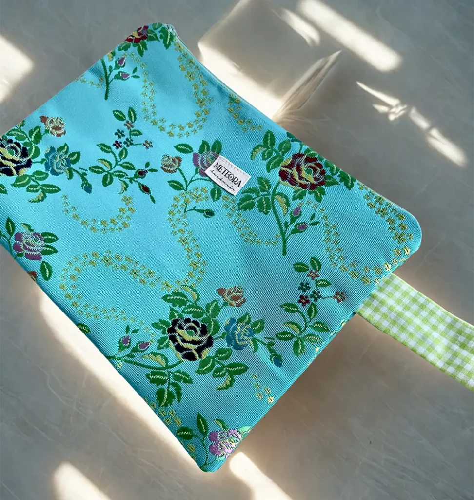 Neceser plano de tela azul turquesa con estampado floral verde y rosa de Meteora Handmade.