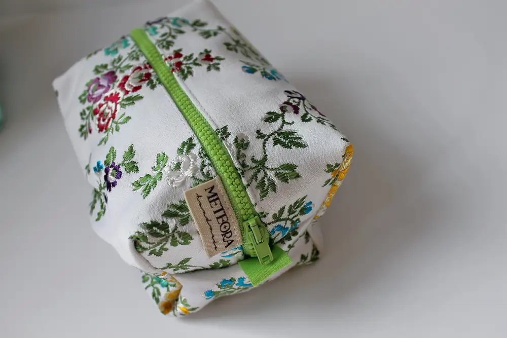 Neceser cuadrado de tela blanca con estampado floral multicolor y cremallera verde de Meteora Handmade.