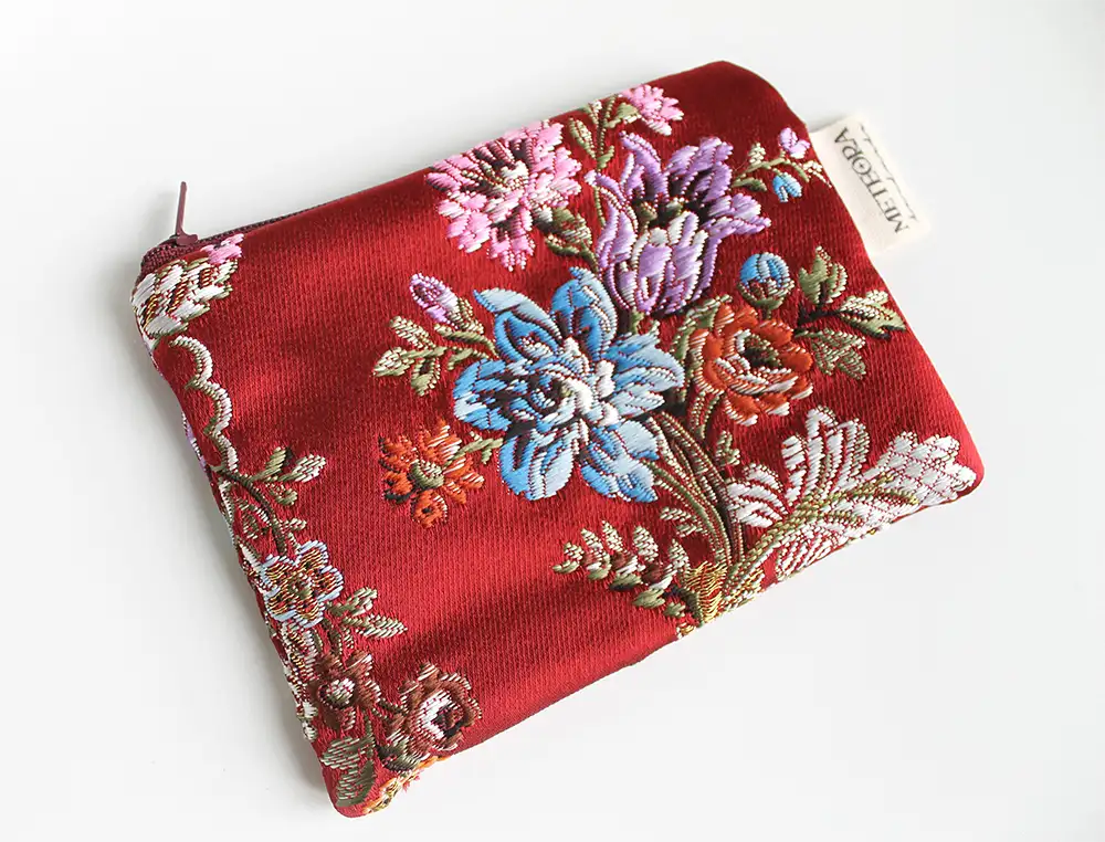 Neceser de tela artesanal en color rojo con bordado floral azul, rosa y verde de Meteora Handmade.